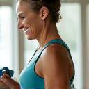 A confident woman in her 40s performing light weights in a bright home gym setting, demonstrating fitness and strength